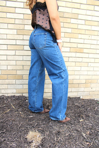 A person shown from the side wearing JBD Square Patch Pocket Straight Jeans, a satin brown with black polka-dot tops, and brown shoes.