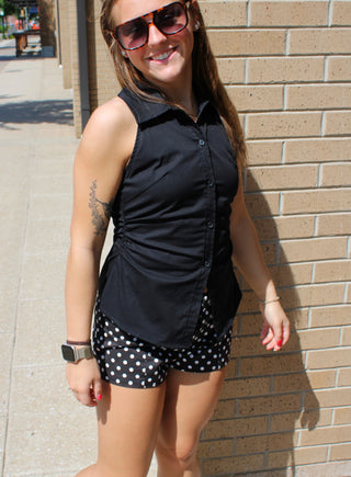 Woman wearing a black sleeveless collared top with ruching and button front detail.