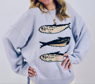 Woman wearing a light blue knit sweater with three sardine graphics on the front.
