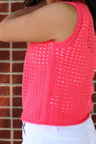 Women's breathable mock neck knit tank in neon pink styled with crisp white pants and gold accessories.