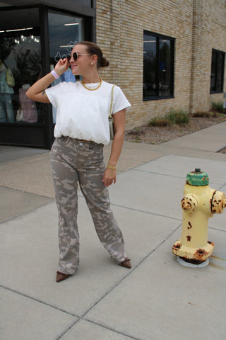 Woman wearing neutral tan camo high-rise dad jeans with a white bubble hem top.