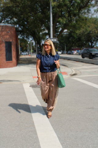 A woman walking on a city street crosswalk wearing Luna Lace Satin Balloon Pants styled with dark denim top, carrying a green tote bag.