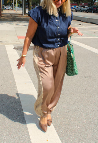 A woman walking on a city street crosswalk wearing a navy blue short-sleeve button-up shirt, mocha satin balloon pants styled for fall, and carrying a green patterned tote bag.