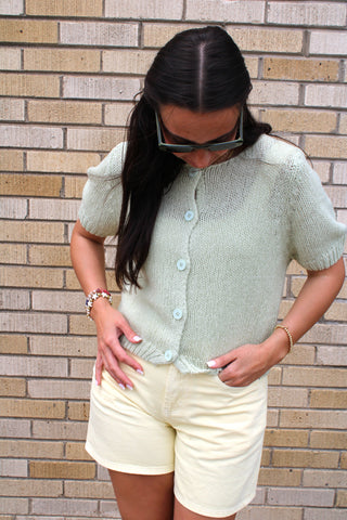 Woman wearing soft sage short sleeve knit cardigan with butter yellow shorts