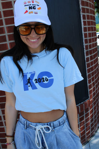 White cropped graphic tee featuring "Meet Me in KC 2026” soccer-inspired design styled with light wash drawstring denim shorts and a KC trucker hat