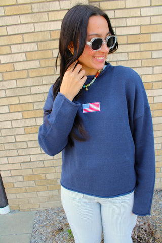 Woman wearing a navy lightweight sweater with embroidered American flag detail