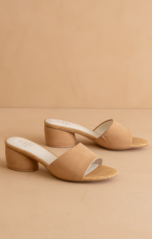 Pair of neutral block heel slide sandals with open toe and raffia-wrapped insole detail on a beige background.