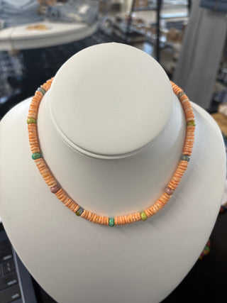 Orange puka shell necklace with mixed turquoise and earthy accent beads displayed on a white bust stand, beach-inspired jewelry
