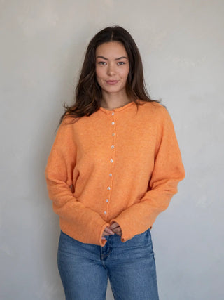 Person wearing an orange cardigan sweater and blue jeans against a plain background