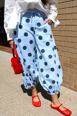 Light blue balloon pants with navy polka dots, featuring a relaxed fit, drawstring waist, and cuffed hem styled with a white blouse and red flats