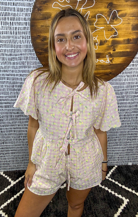 Woman wearing a pastel pink gingham short set with yellow floral print and tie-front bow details, styled for a cute and feminine summer boutique look