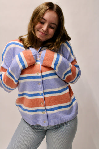 Woman wearing a pastel striped button front cardigan in periwinkle, coral, and blue tones.