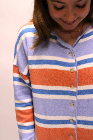 A close-up of a woman wearing a fuzzy, colorful, knit, button front cardigan with horizontal stripes in lavender, orange, and white, featuring a button-up front.