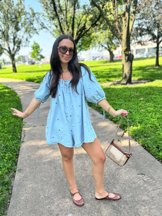 Woman wearing a light wash embroidered denim romper with colorful floral details and puff sleeves
