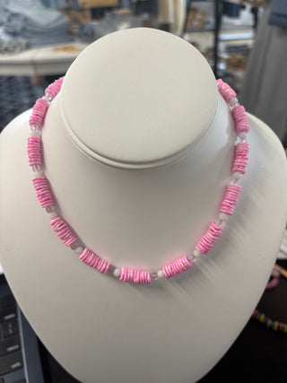 Pink puka shell necklace with white spacer beads displayed on a white bust stand, boutique summer jewelry