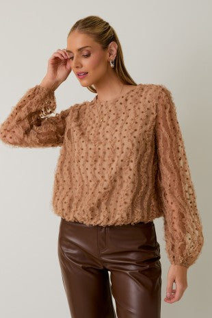 Woman wearing a brown textured top and leather pants against a plain background