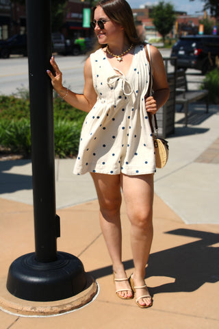 Women's cream denim romper with navy polka dots, a tie-front neckline, and a relaxed babydoll fit.