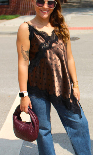A woman wearing a sheer brown polka-dot camisole top with black lace trim, paired with blue jeans and holding a burgundy textured handbag.