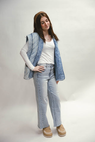 Woman wearing a denim vest, white shirt, and light blue jeans on a plain background