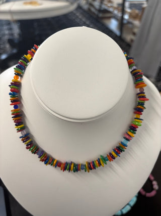 Rainbow puka shell necklace with multicolor disc beads displayed on a white bust stand, vibrant summer jewelry