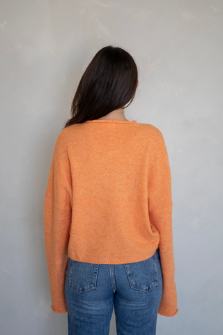 Person wearing an orange cardigan sweater and blue jeans against a plain background