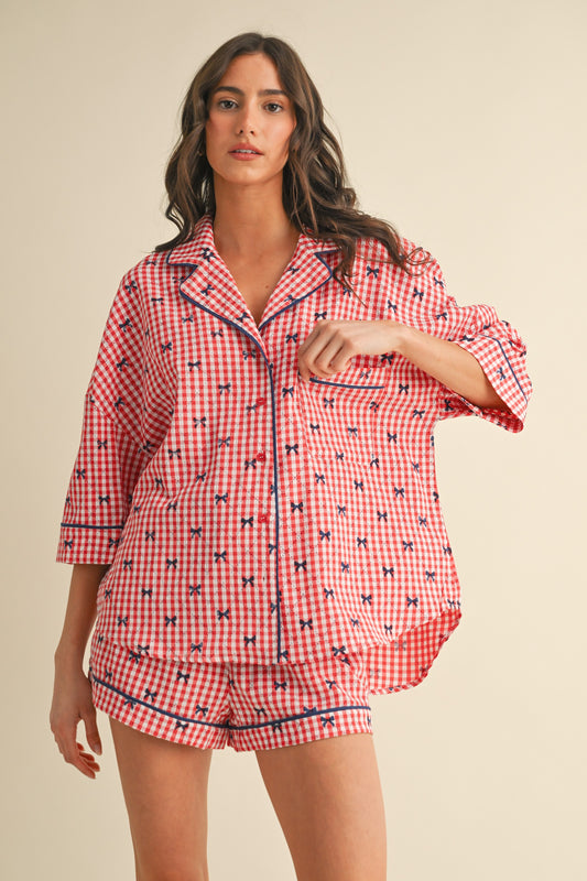 Woman wearing a red and white gingham pajama set with navy blue embroidered bows, button-up top, and matching shorts – patriotic sleepwear for women