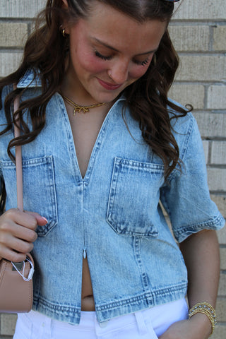 Light wash denim V-neck top with cropped fit and front pockets styled casually