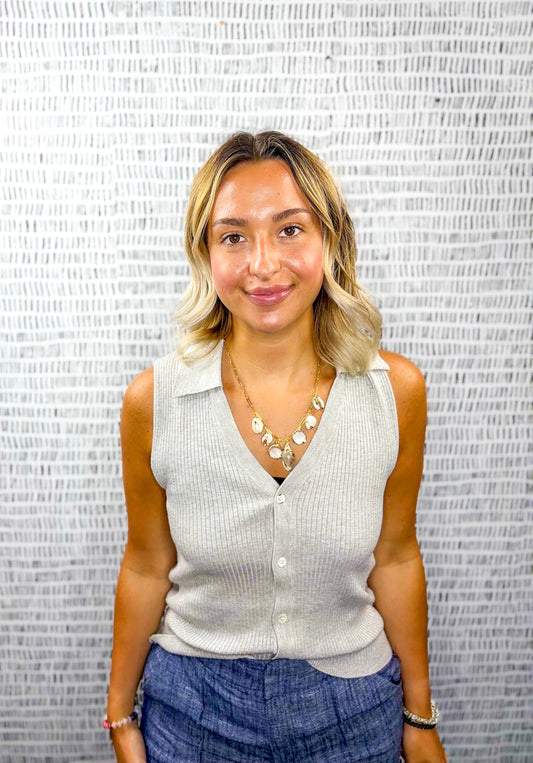 Woman wearing a ribbed grey sleeveless collared top with a button front, paired with blue chambray shorts and a gold shell necklace