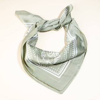 Sage green silk bandana-style scarf with white paisley print, folded and tied in a chic knot