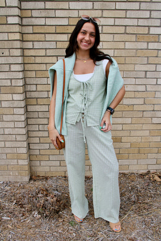 Woman in a light green outfit standing against a brick wall.