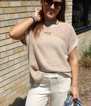 Woman wearing neutral open knit sweater with relaxed coastal-inspired styling.