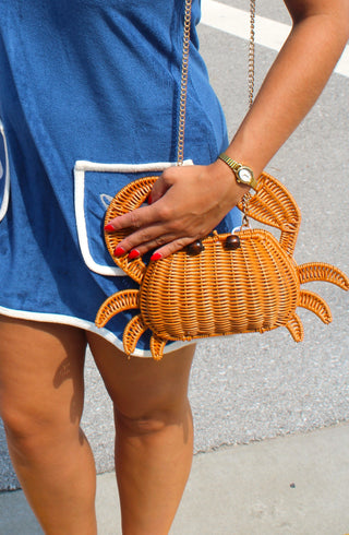 Sebastian Woven Crab Clutch Bag featuring a handwoven rattan crab design with a removable gold chain strap, styled with a navy dress for a coastal summer look.