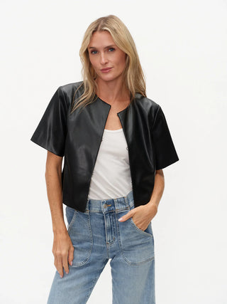 Woman wearing a black leather jacket, white top, and blue jeans on a light gray background