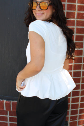White bubble peplum top with a fitted bodice, square neckline, and voluminous hem paired with black pants.