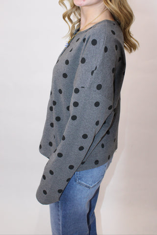 Person wearing a gray polka dot cardigan on a plain background