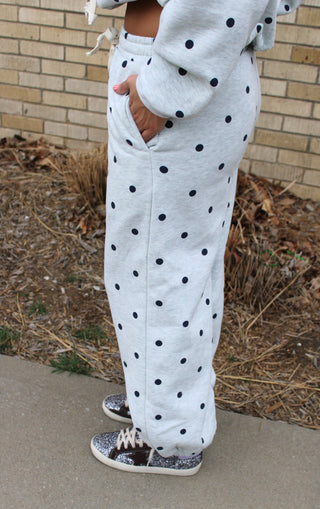 woman wearing gray sweatpants with navy polka dot standing on a sidewalk with a brick wall background.