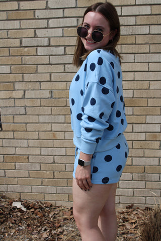 Sideview of a woman wearing a blue sweatshirt with navy polka dots and matching lounge shorts.