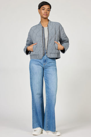 Woman wearing a gray quilted bomber jacket and  jeans on a white background
