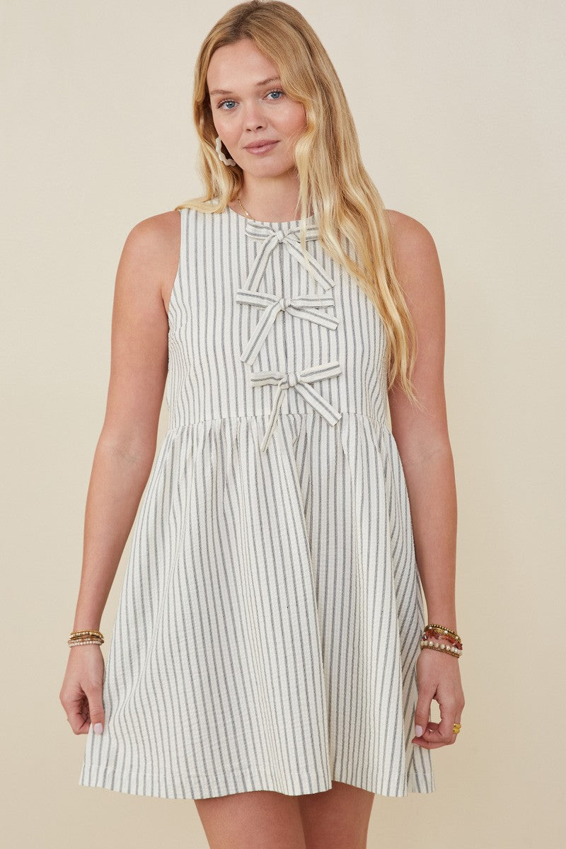 Woman wearing a sleeveless ivory and grey striped mini dress with three front bow tie details – boutique summer dress style
