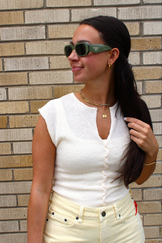 Women's cream sleeveless knit top with a V-neckline and button front styled with pastel yellow shorts.