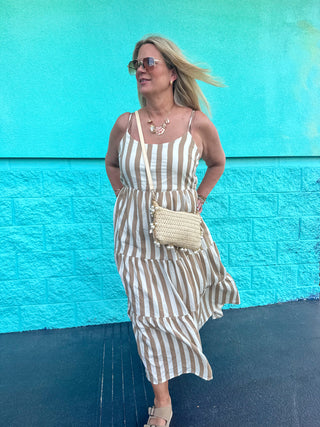 Woman wearing a tan and white striped tiered maxi dress styled with neutral accessories, standing against a turquoise wall