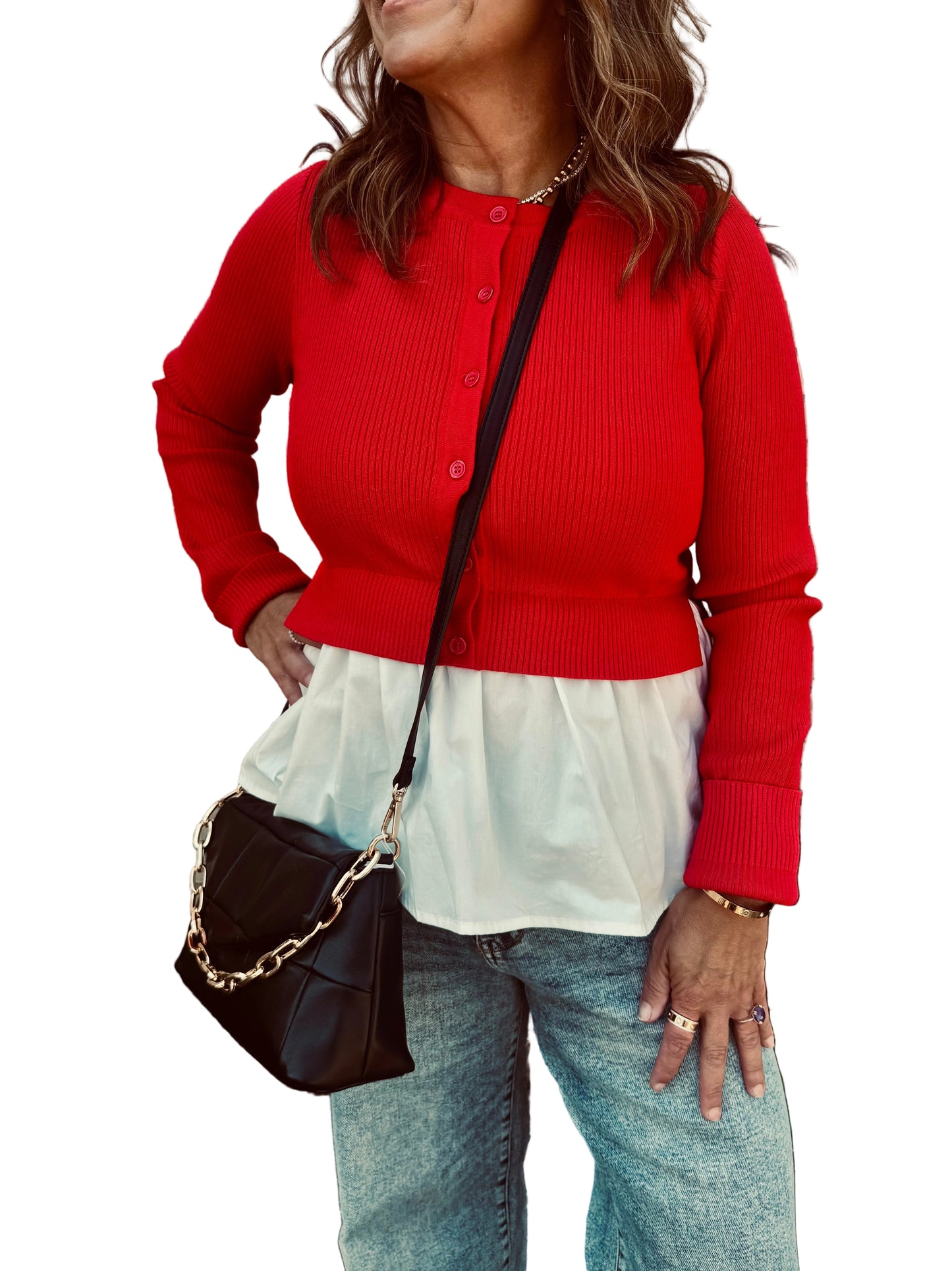 Person wearing a red cardigan over a white top with blue jeans, standing against a brick wall.