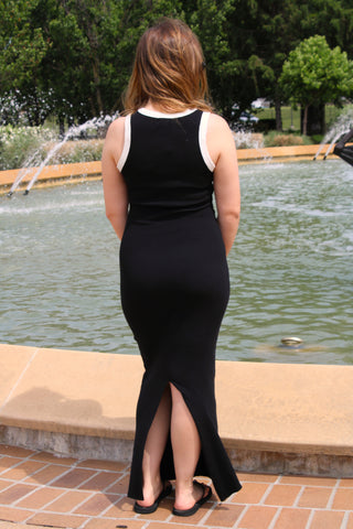 Back view of black ribbed maxi dress featuring contrast trim and back slit detail.