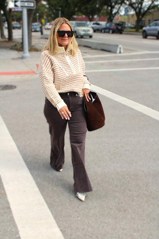 A woman walking on a city street wearing Blair sweater open knit texture and contrast trim detail, dark brown flared denim Dear John pants, and carrying a brown leather tote bag.